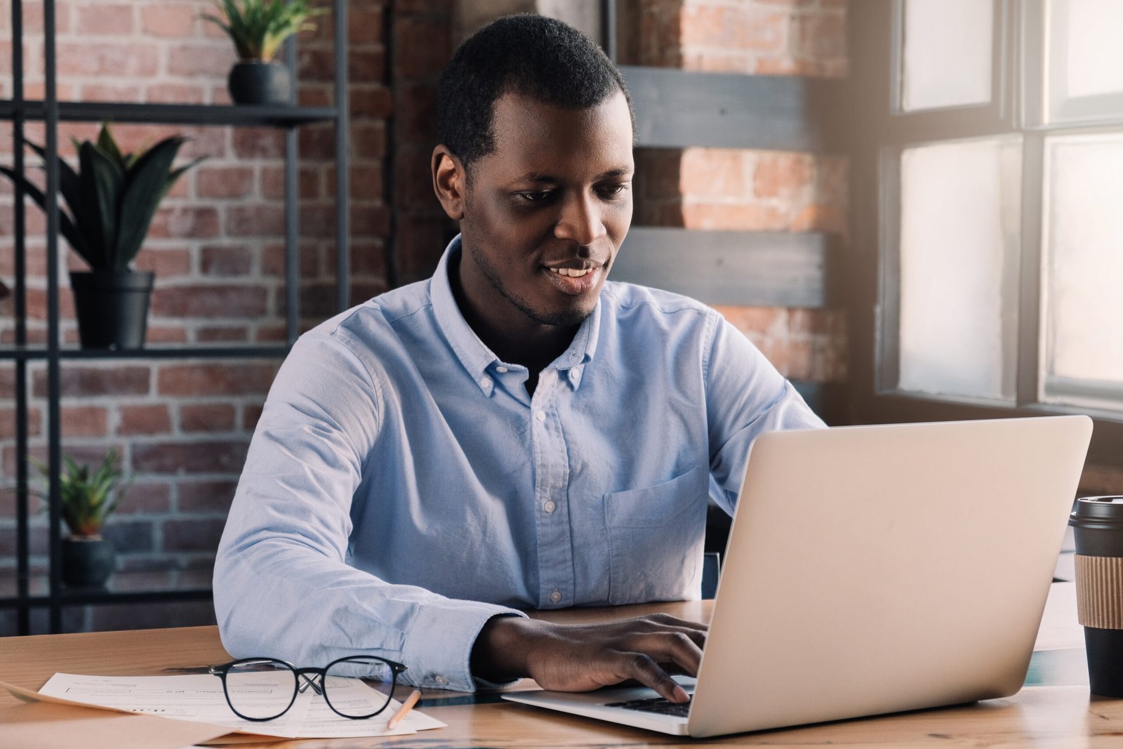 Young african american business man sitting in loft office or cafe, working on new online IT startup project, using laptop
